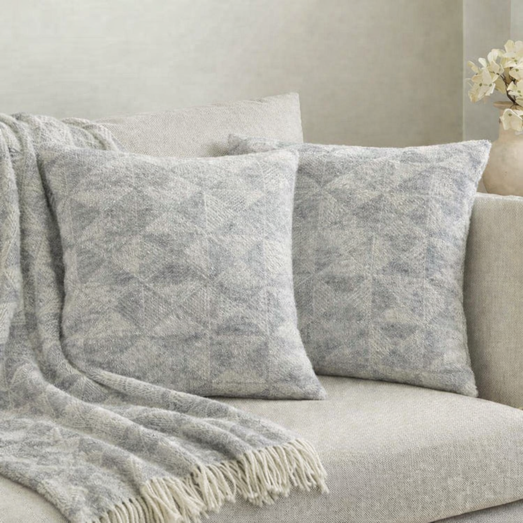 Gray textured throw blanket and pillows on a beige sofa with a neutral background