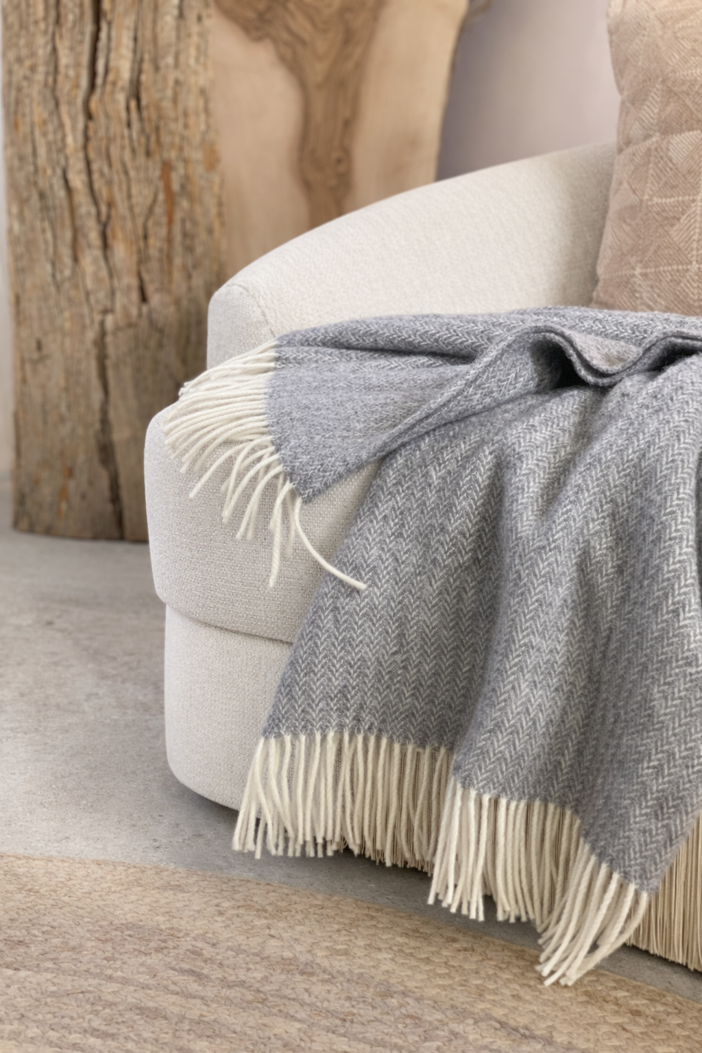 Gray blanket with white fringe draped over a beige armchair against a wooden wall.